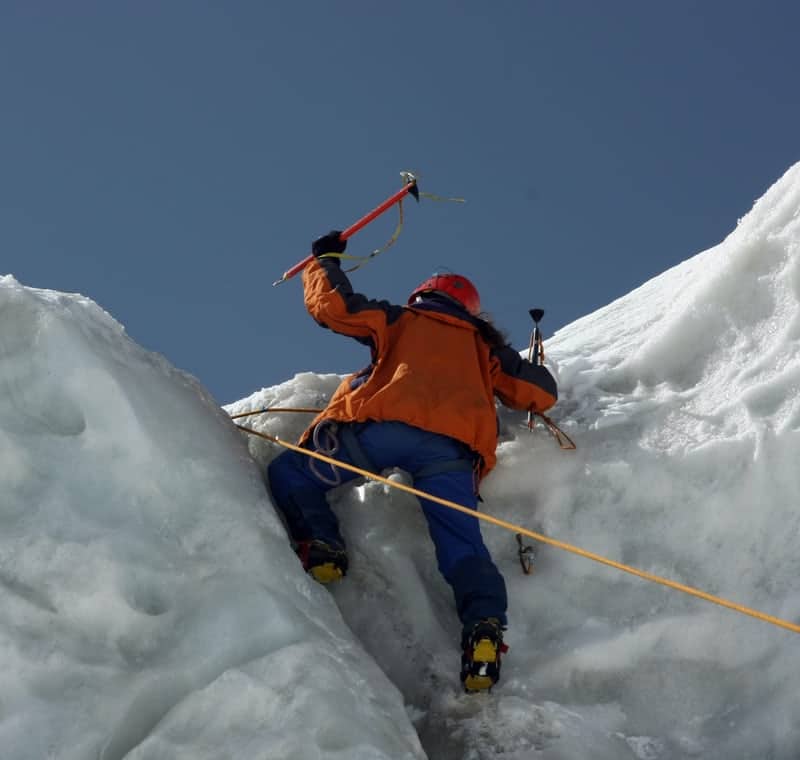 Alpiniste avec des piolets qui crampons qui franchis un obstacle en montagne
