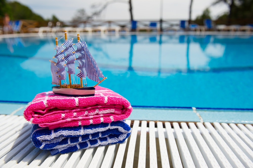 deux serviettes pliées avec un petit bateau en jouet posé dessus au bord d'une piscine dans un camping parc aquatique