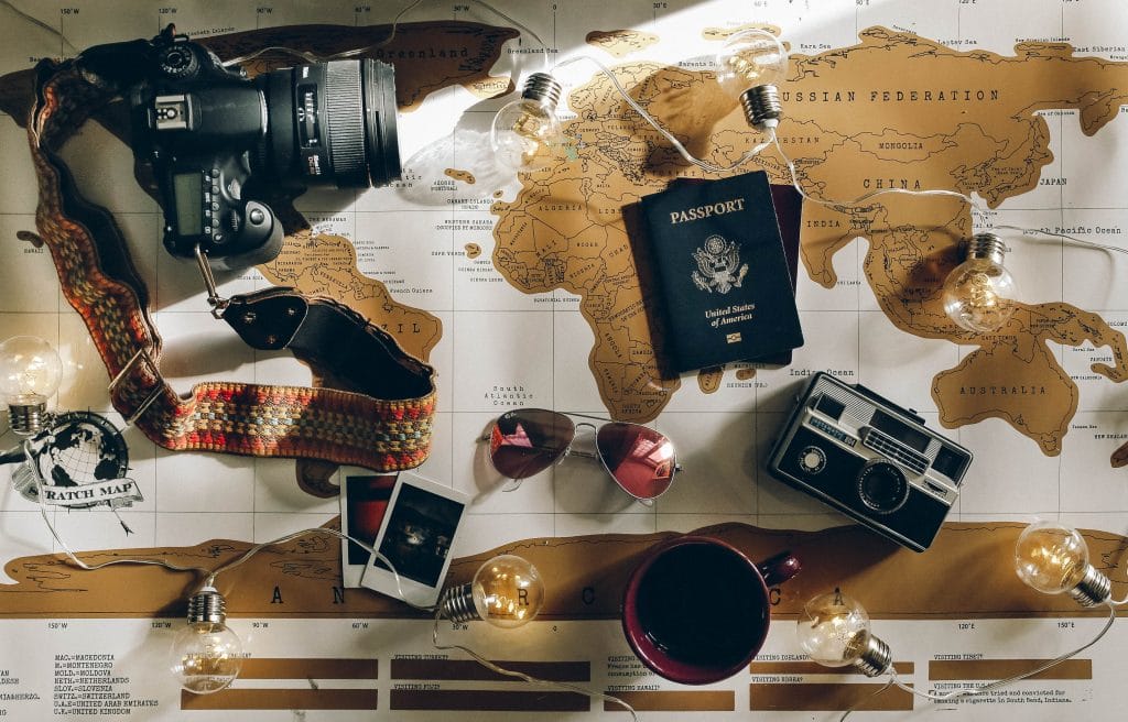Carte du monde vintage où sont disposés des accessoires pour voyageurs (appareil photo, lunettes de soleil, passeport)