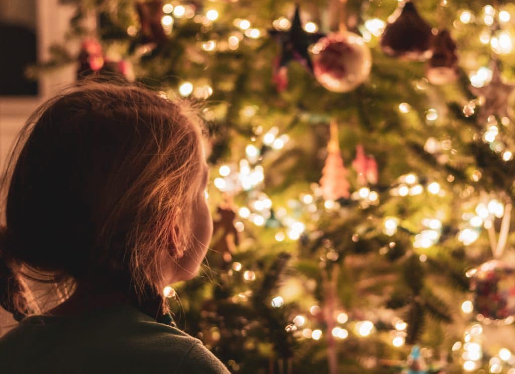 Petite fille s'émerveillant devant un sapin de Noël éclairé