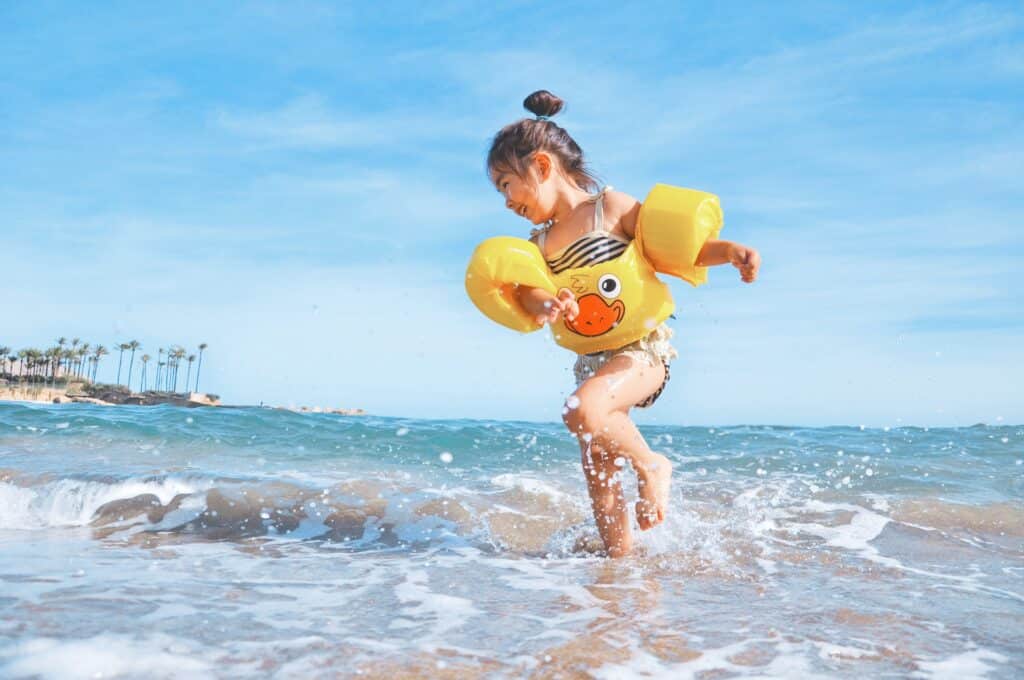Petite fille s'amusant sur le bord de mer avec des brassards flotteurs jaunes